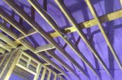 looking up at wooden framing and purple spray foam insulation inside house