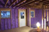 purple spray foam insulation applied to walls of cabin between wooden framing