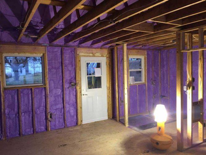 purple spray foam insulation applied to walls of cabin between wooden framing