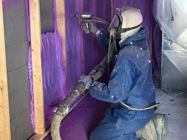 man in blue suit with gas mask applying purple spray foam to wall