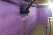 purple spray foam applied around pipes on basement walls